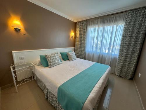 a bedroom with a bed with blue pillows and a window at RF La Quinta Park Suites in Santa Úrsula