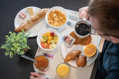 カルクフーにあるHôtel Inn Design Resto Novo Carquefouの朝食の食べ物を載せたトレイを持ってテーブルに座っている男性