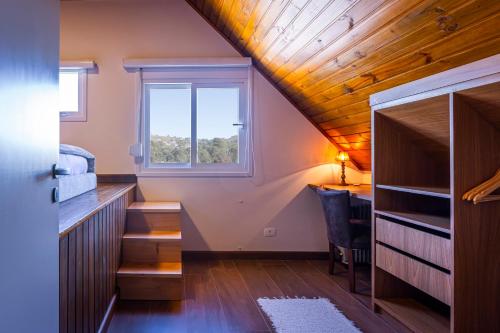 a small attic room with a desk and a window at Zur Suítes in Campos do Jordão