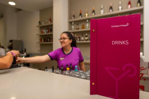 a woman standing behind a counter with a pink drink dispenser at Holiday Village Türkiye in Dalaman