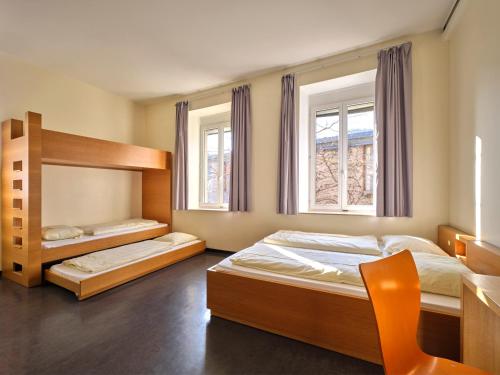 a bedroom with two beds and a chair and two windows at Youth Hostel Schengen / Remerschen in Remerschen