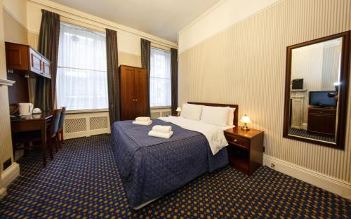 Cette chambre comprend un lit, un bureau et un miroir. dans l'établissement Regency House Hotel, à Londres