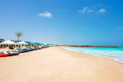 a beach with a line of umbrellas and the ocean at Gewan Palace New Alamein in El Alamein