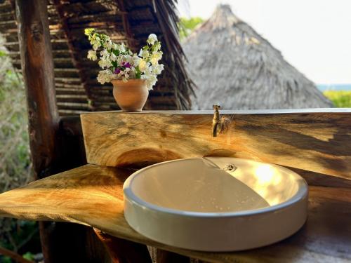 a sink on a wooden counter with a vase of flowers at Chole Mjini Treehouses Lodge in Utende