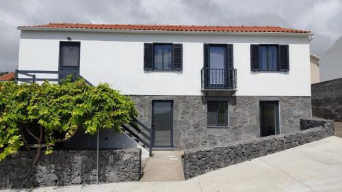 a white house with black windows and a stone wall at Quinta do Araçal T1 in Horta