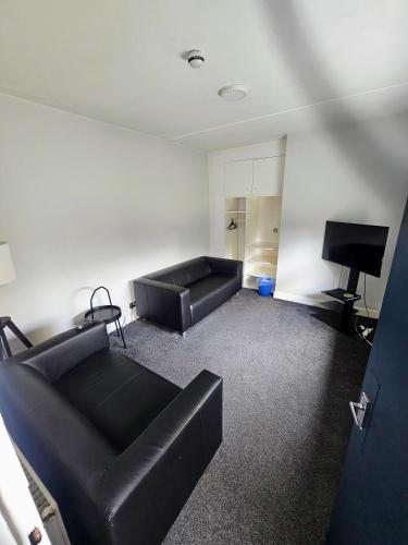 a living room with black leather furniture and a flat screen tv at Cunninghame House in Beith
