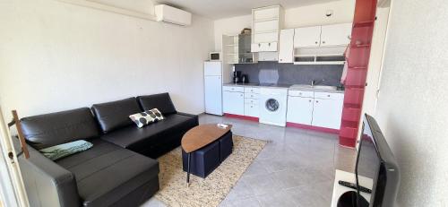 un salon avec un canapé noir et une cuisine dans l'établissement F1 Cosy 45m2, 2 mn mer, du port, cœur ville, à La Grande Motte