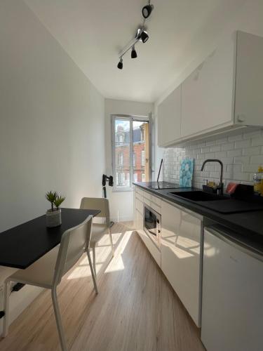 une cuisine avec des armoires blanches, une table et un évier dans l'établissement ​Cœur de ville ! Cœur de l'Oise​​ ! Moderne & fonctionnel​, à Clermont