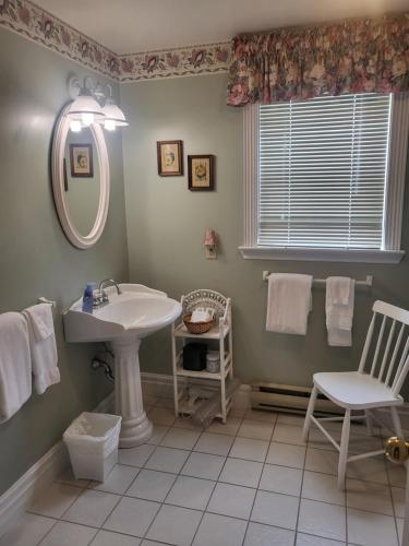 a bathroom with a sink and a mirror and a chair at Cranberry Cove Inn in Louisbourg