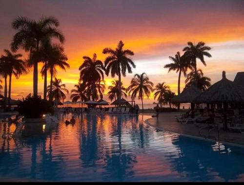 ein Resortpool mit Palmen und Sonnenuntergang in der Unterkunft Zuana Beach Resort -Semana 37 in Playa Dormida