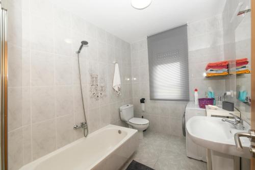 a bathroom with a tub and a toilet and a sink at Apartamento O Cruceiro in A Pobra do Caramiñal