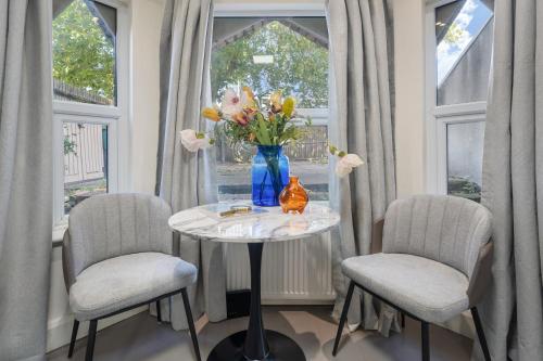 a table with a vase of flowers and two chairs at Leamington Park Studio with Parking in London