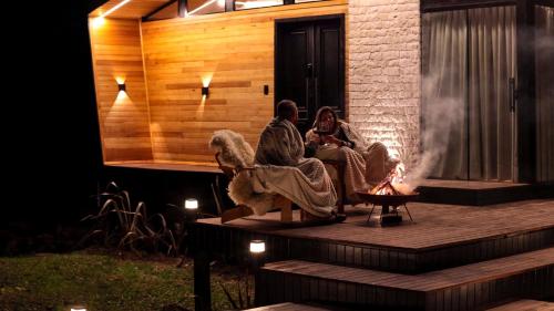 two people sitting on a deck next to a fire at SEGREDO do VALLE - BOSQUE in Urubici
