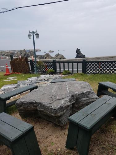 two picnic tables and a large rock next to the ocean at Ulsan Lighthouse Pension in Ulsan