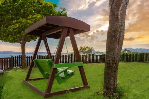 a green swing sitting next to a tree at Namhae New Island Pension in Namhae