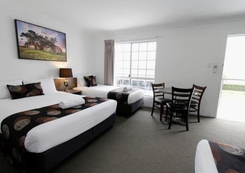 Una habitación de hotel con dos camas y una mesa y sillas. en Takalvan Motel, en Bundaberg