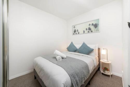 a white bedroom with a bed with blue pillows at Sensational City Apartment with Lake Views in Canberra