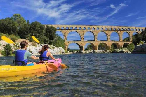 un homme et une femme dans un kayak sur une rivière avec un pont dans l'établissement Le Vendome, à Nîmes