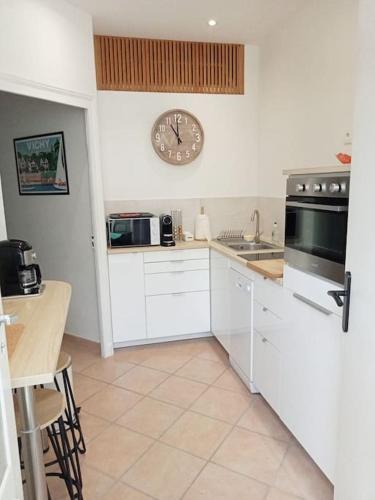 une cuisine avec des placards blancs et une horloge murale dans l'établissement Le Petit Appart au coeur de Vichy, à Vichy