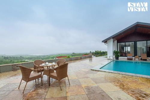 Un patio con mesa y sillas junto a una piscina. en StayVista at Whispering Meadows - Pool, AC & View, en Nashik