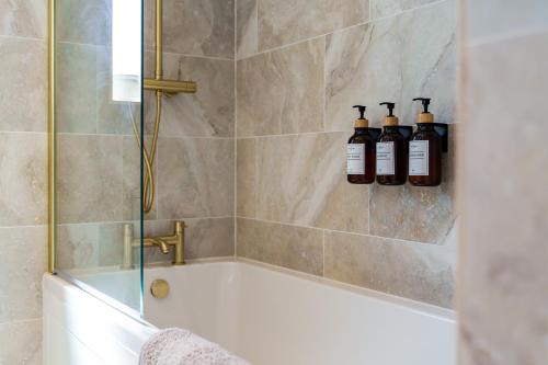 a bathroom with a bath tub with three bottles on the wall at Bungalow Close to South Downs & Beach in Angmering