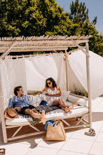 un homme et une femme assis sur un lit sous un gazebo dans l'établissement Slow Village Marennes Oléron, à Marennes