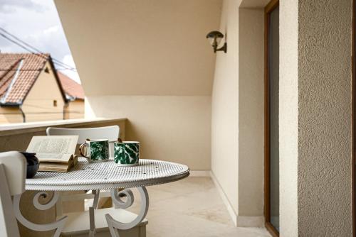 a table with a book and mugs on a balcony at Sika Grand Palladium Garden & Spa Central Apartment Arad in Arad