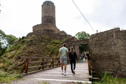 a man and a woman walking on a bridge with a tower in the background at Pytloun Wellness Hotel Hasištejn in Místo