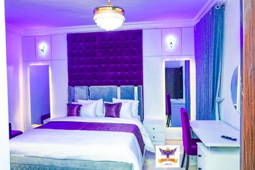 a purple bedroom with a large bed and a desk at Queen Esther's Luxury Apartment in Ankuru