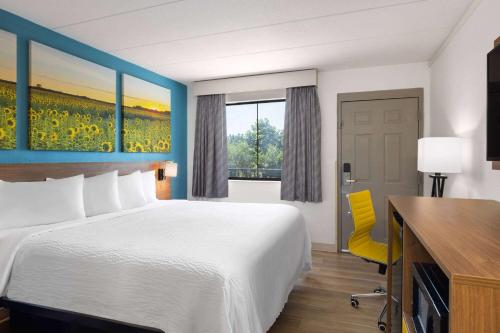 a hotel room with a bed and a desk and a window at Day's Inn & Suites by Wyndham Indianapolis Airport East in Indianapolis