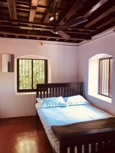 a bedroom with a bed with blue sheets and two windows at Neermathalam, a traditional kerala tharavadu in Palakkad