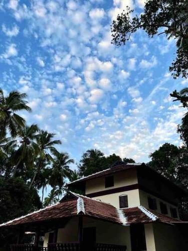 a building with palm trees and a cloudy sky at Neermathalam, a traditional kerala tharavadu in Palakkad