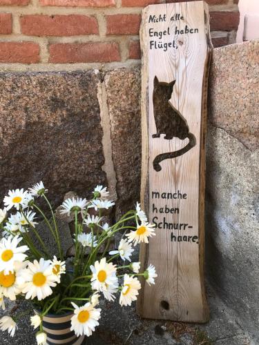 a wooden sign with a cat on it next to flowers at Bauerhof Kleingarn - Bauernhus 11 in Sulsdorf auf Fehmarn