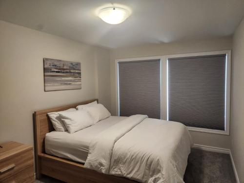 a bedroom with a bed with white sheets and two windows at Stay with Star in Ottawa