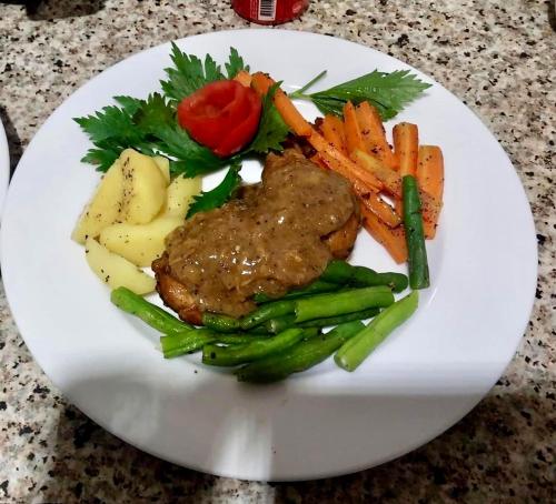 a white plate with meat and vegetables on a table at Rivorich Residence Kandy in Kandy