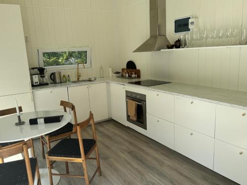 a kitchen with white cabinets and a table and a stove at Cabin in the forest with Spa bath in Västra Torup