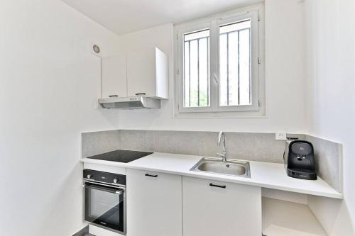 une cuisine blanche avec un évier et une fenêtre dans l'établissement Magnifique studio banlieue Parisienne - Montreuil, à Montreuil