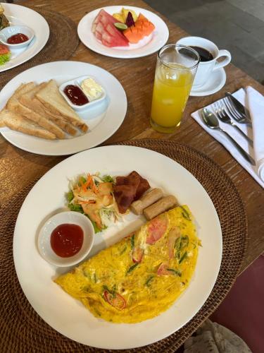 een tafel met borden ontbijtproducten en een glas sinaasappelsap bij Abitama Villa in Ubud