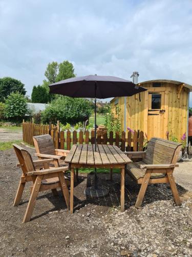 a picnic table and two chairs with an umbrella at Poachers Keep, Shepherds Hut in Endon
