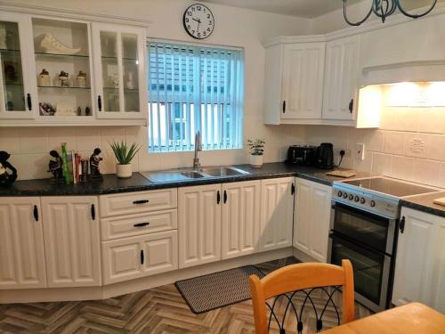 eine Küche mit weißen Schränken und einer Uhr an der Wand in der Unterkunft Mountainview Cottage in Dungiven