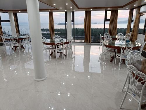 a dining room with white chairs and tables and windows at Quan Lan Nam Phong Hotel in Quan Lạn