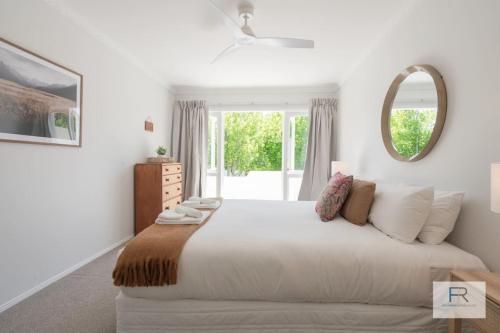 a white bedroom with a large bed and a mirror at QV Stays Gorgeous Hideaway with Spanish Charm in Auckland