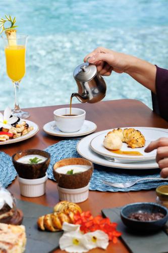a table with food and a person holding a tea kettle at Almareia Boutique Hotel in Praia dos Carneiros