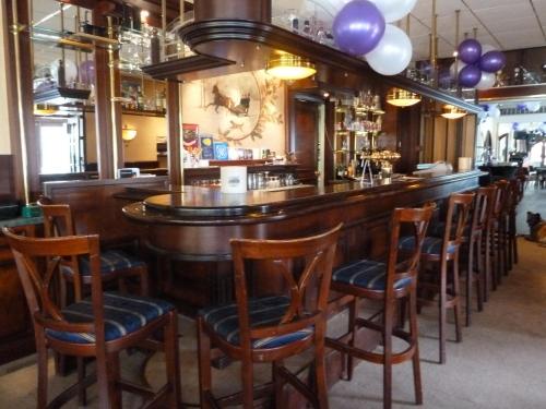 a bar with a row of wooden bar stools at Hotel Het Landhuis in Oldenzaal