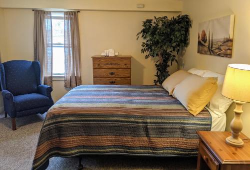 a bedroom with a bed and a blue chair at Casual Living Extended Stay Hotels in Algonquin