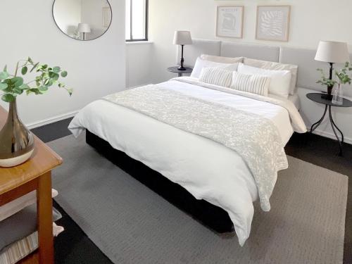 a white bedroom with a large bed with white sheets and pillows at Stylish Executive City Pad w Parking and Pool in Perth