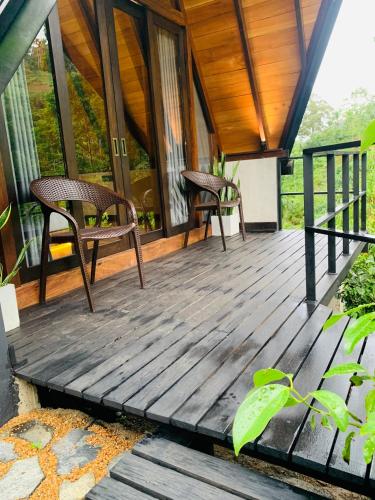 a wooden deck with two chairs on a house at Cannelle Hill Cabanas in Deniyaya