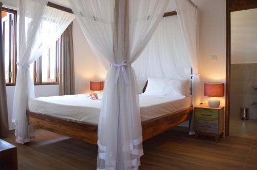 a bedroom with a canopy bed with white curtains at La Perle Appartements in Baie Lazare Mahé