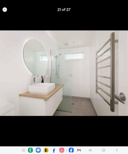 a white bathroom with a sink and a mirror at Waihi beach Toroha cosy cabin in Waihi Beach