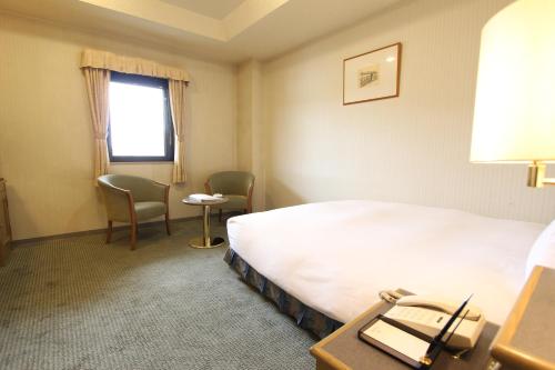 a hotel room with a bed and chairs and a window at Shimonoseki Grand Hotel in Shimonoseki